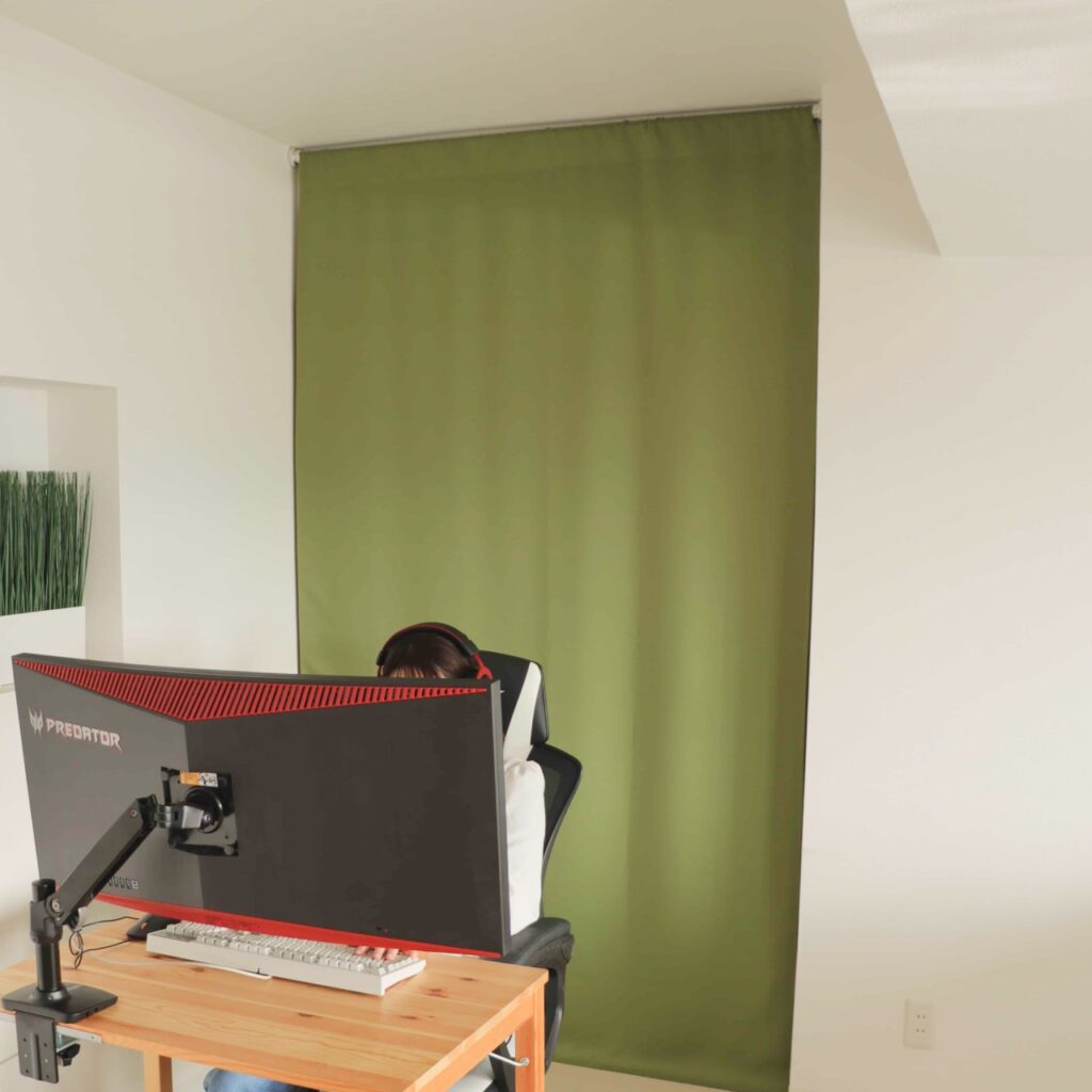 間仕切りとして突っ張り棒で設置できる防音カーテンパーテンエバーグリーンがゲームをしている女性の背面の窓に音漏れの防音対策として設置されている